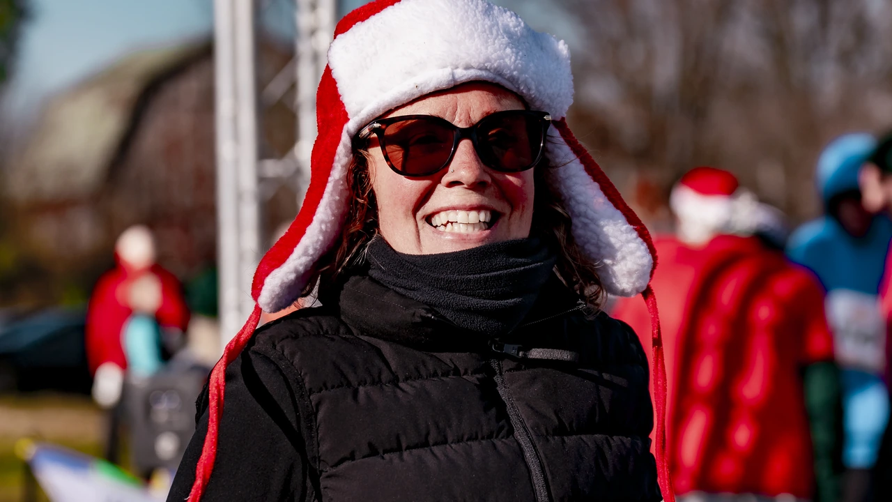 A smiling woman in a Santa hat and sunglasses at an outdoor race