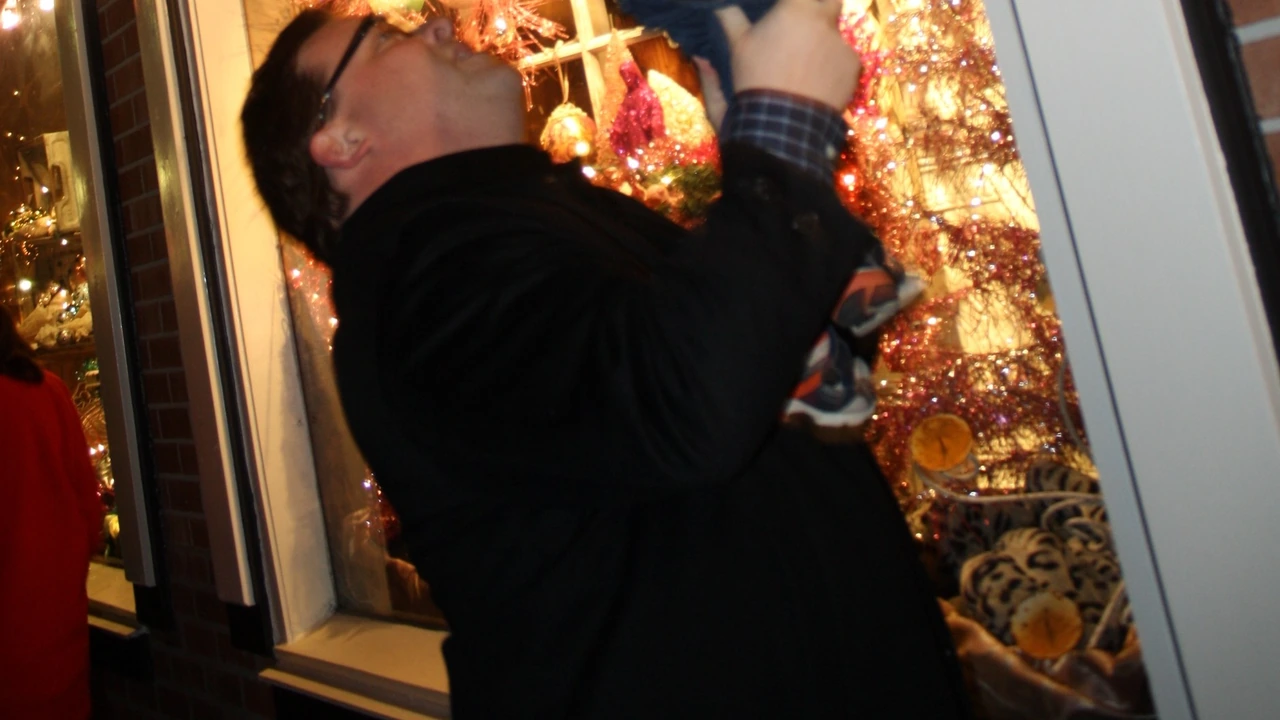 A man reaches up to hang an ornament among glittering decorations
