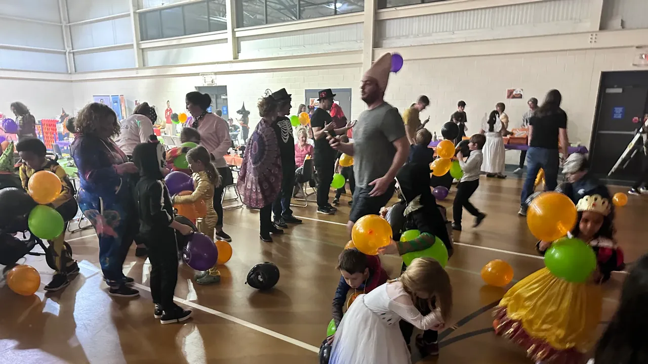 Children in costumes play with balloons in a recreation center gym
