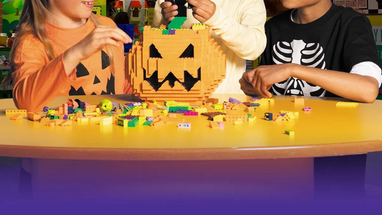 Children build with Lego bricks around a jack-o'-lantern model