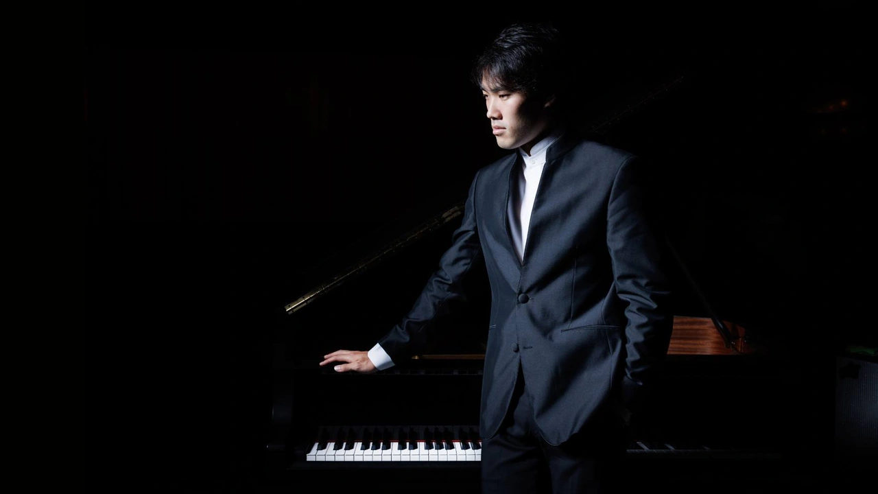 A pianist in a dark suit plays a grand piano on a dark stage