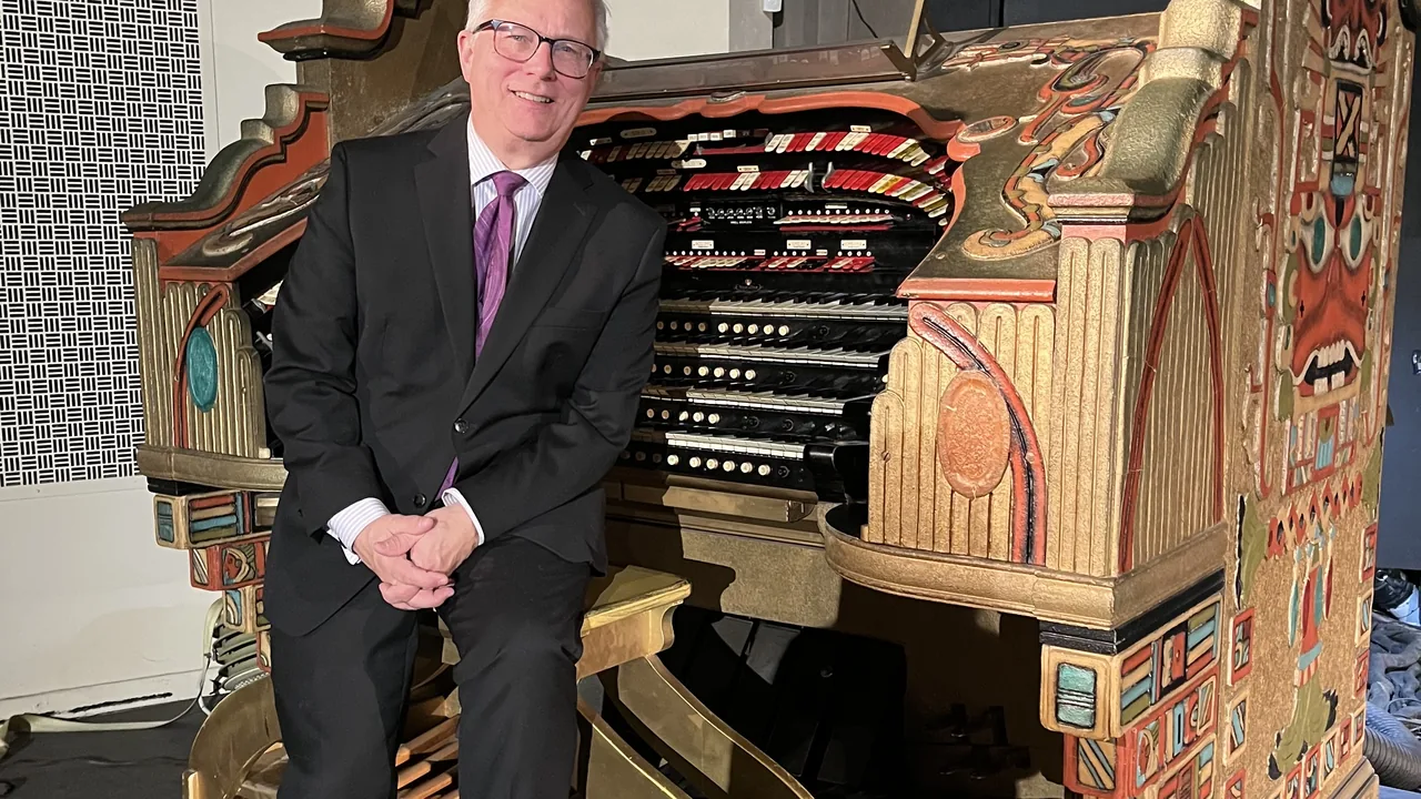 A man in a suit stands beside an ornate theater pipe organ console