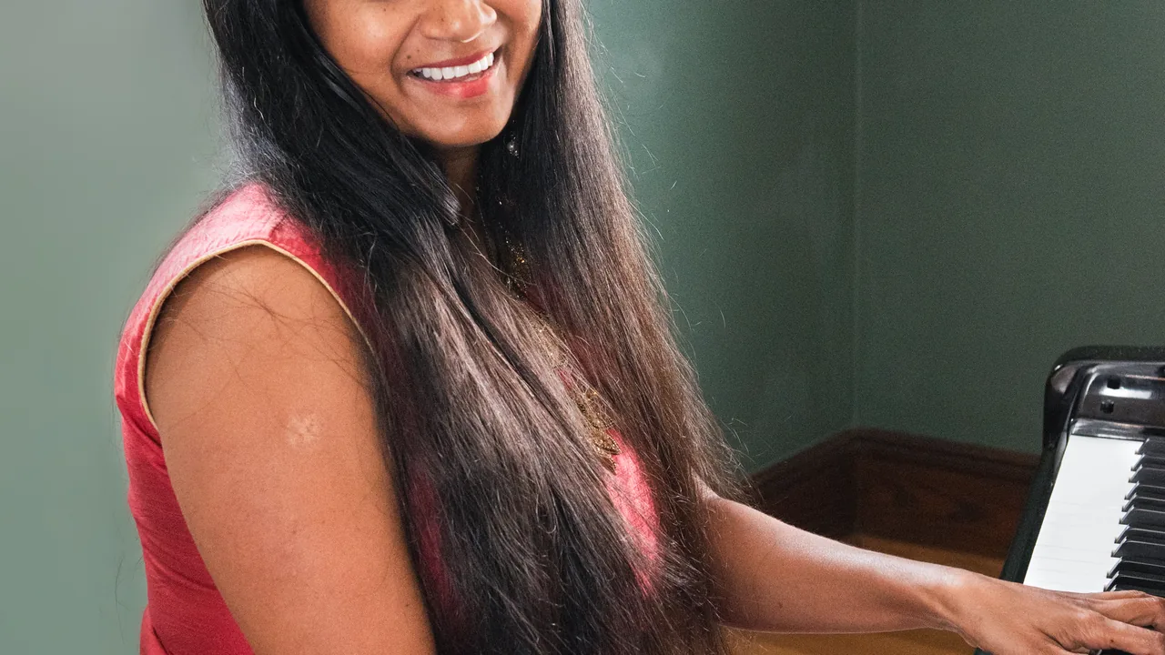 A smiling woman with long dark hair plays piano