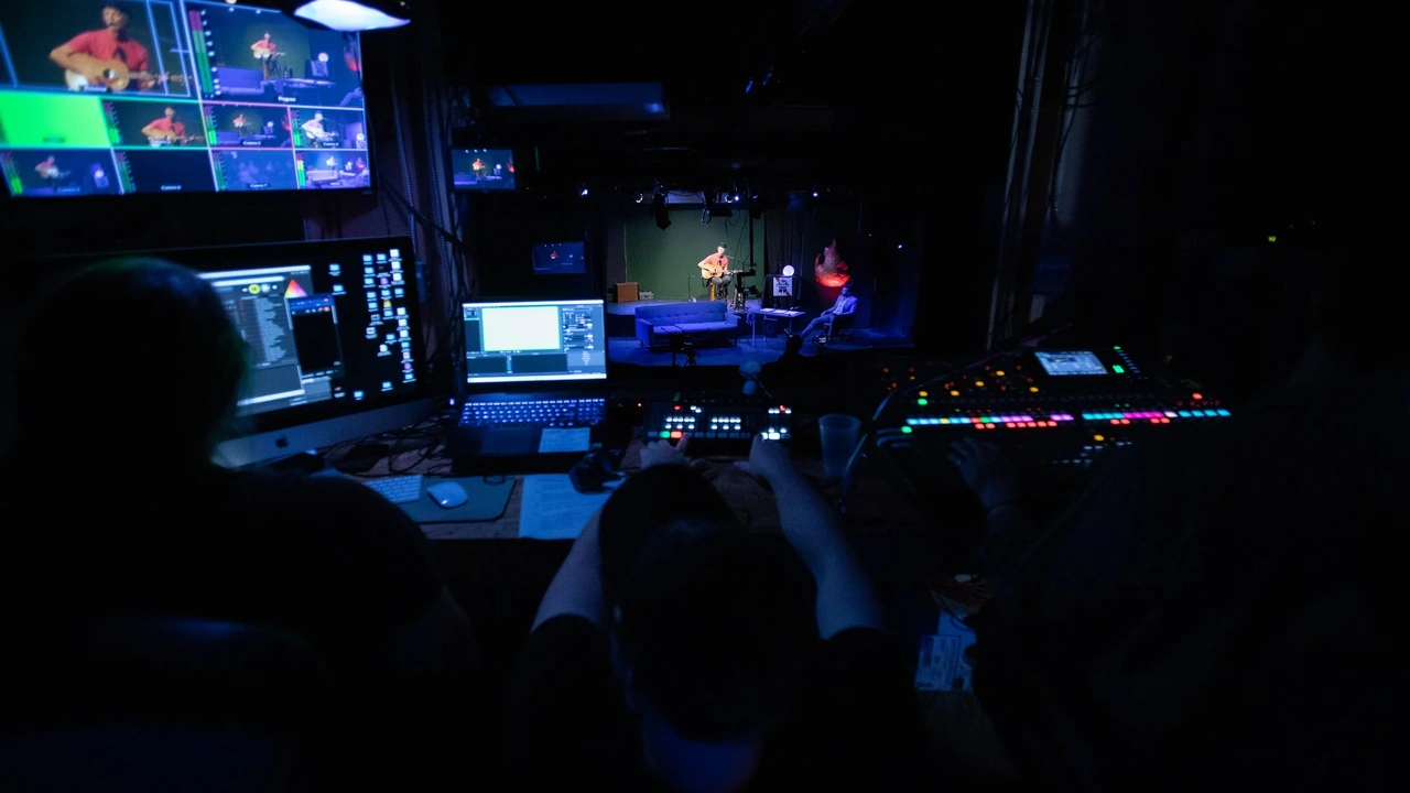 A dim control booth glowing with monitors and mixing gear