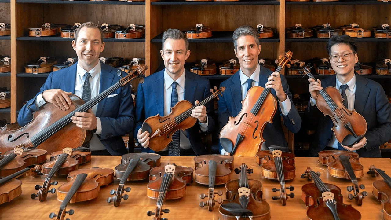 Four string players in suits pose with violins and a cello in a workshop