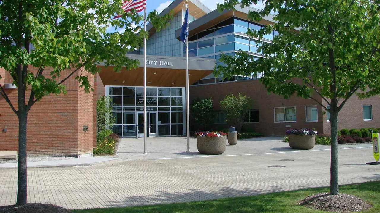 A brick civic building with flags and a tree-lined walk