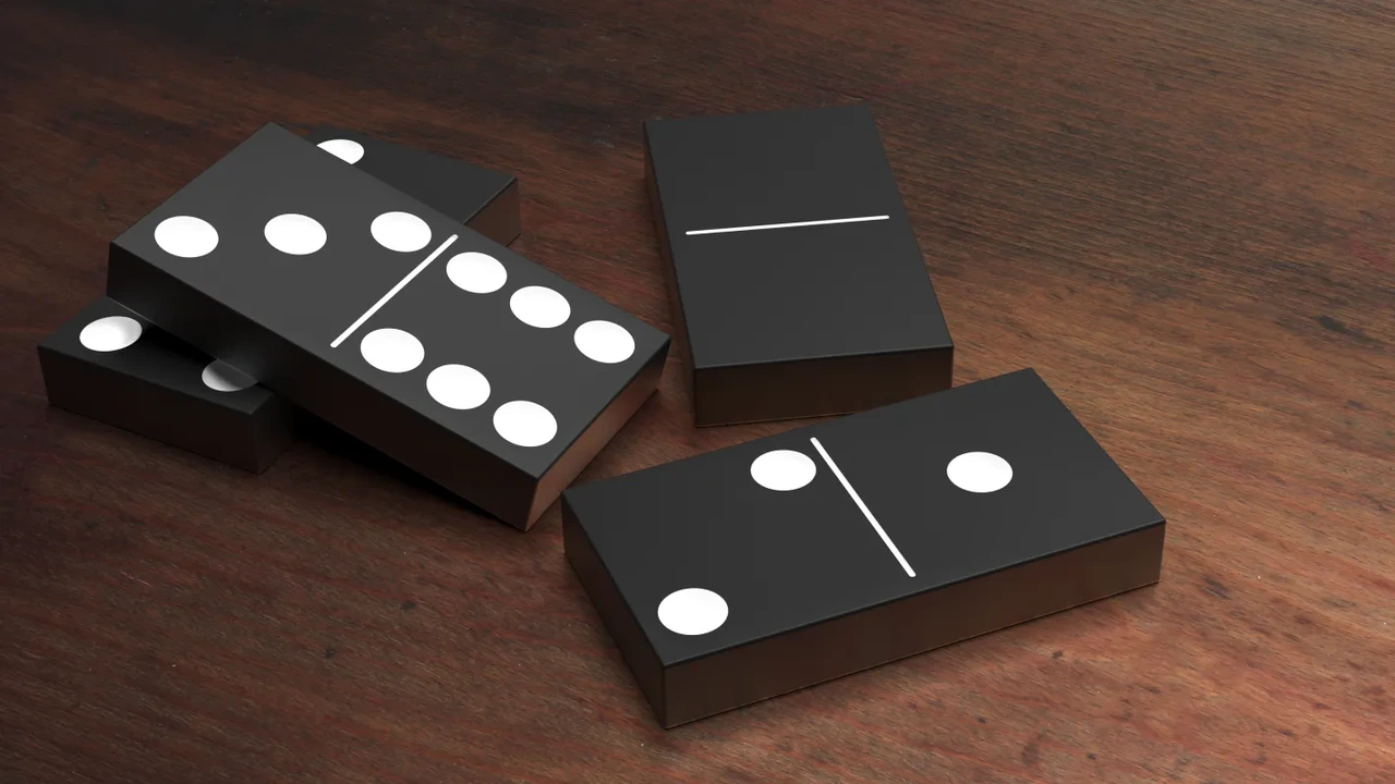 Black dominoes with white pips scattered on a wooden table.