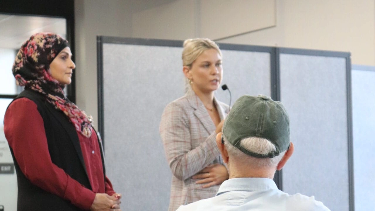 A woman in a headscarf and a woman with a microphone headset speak to a seated guest.
