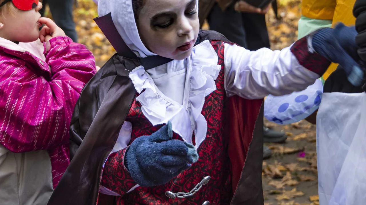 A child dressed as a vampire trick-or-treats among fall leaves