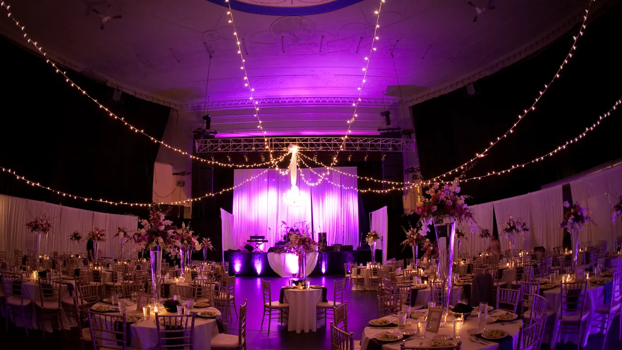 A ballroom lit in purple with string lights and round banquet tables