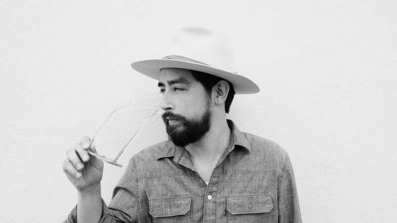 A bearded man in a white hat looks to the side