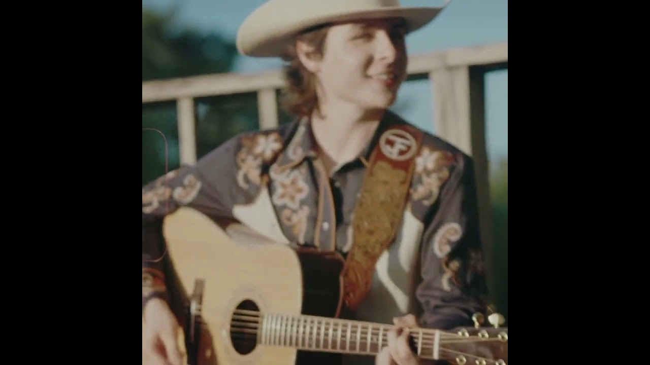 A singer in a cowboy hat plays an acoustic guitar