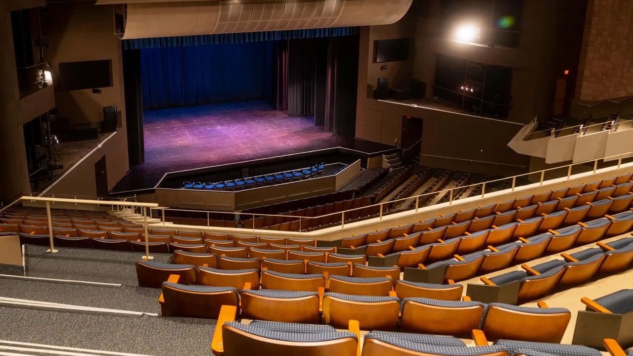 An empty auditorium with orange seats facing a lit stage