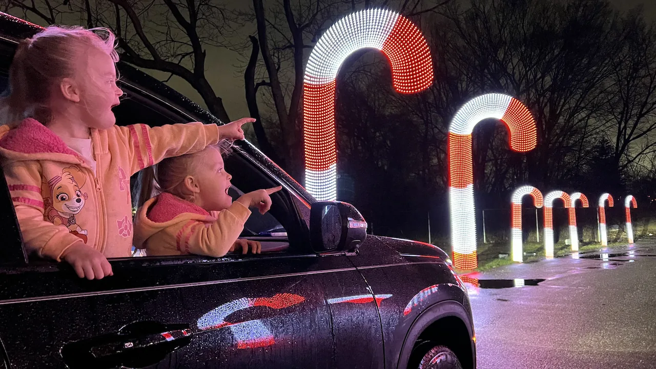 Children lean from a car window toward giant lit candy canes
