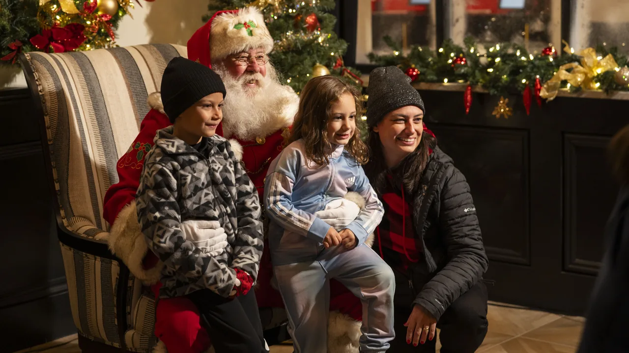 Children sit with Santa beside a decorated mantel