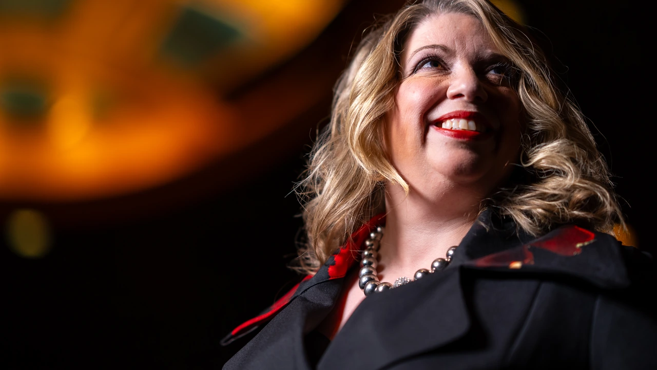 A smiling woman with wavy hair in a dramatic dark coat