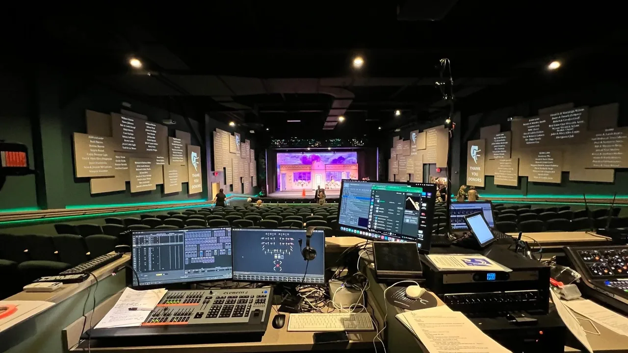 A studio control room with monitors and a mixing desk facing a stage
