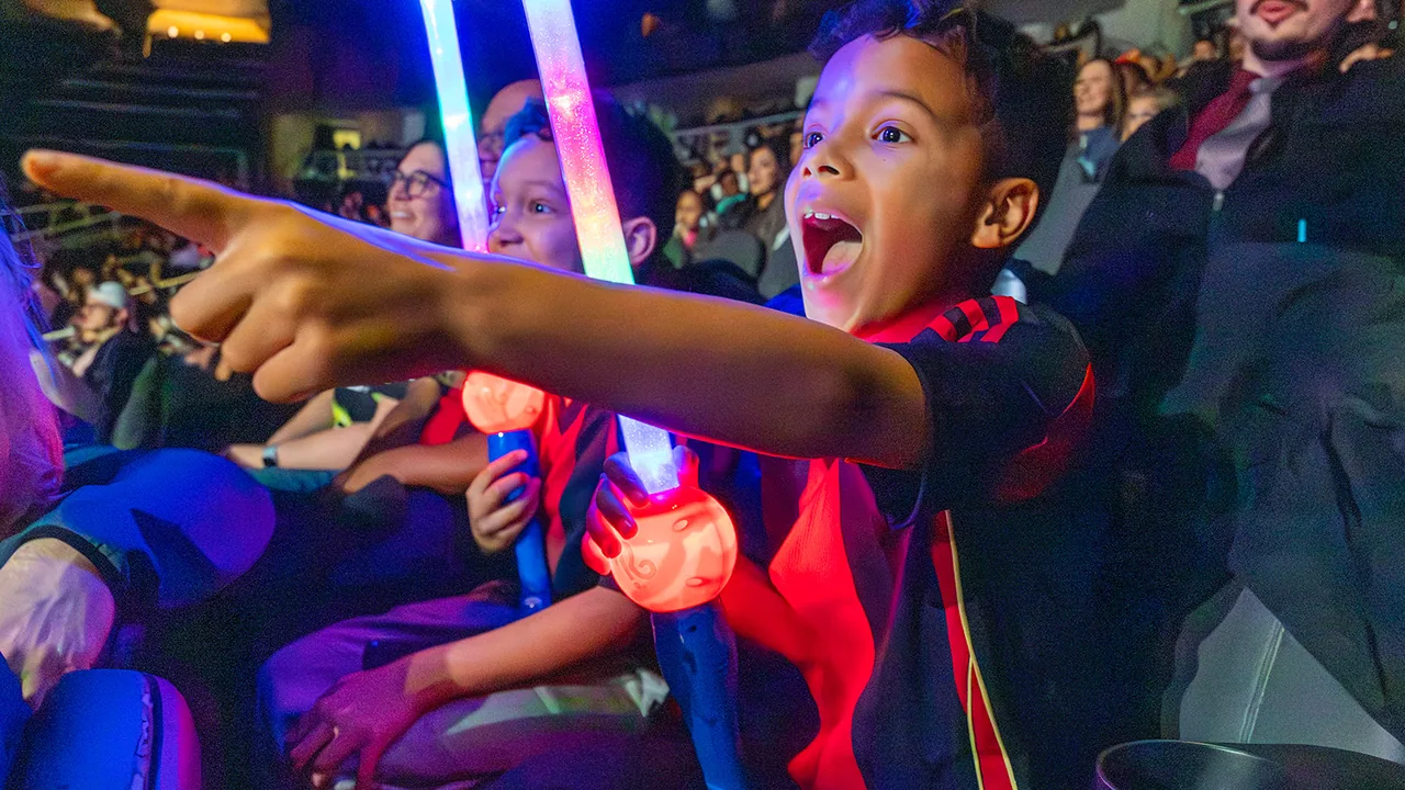 Excited children wave light sabers in an arena crowd