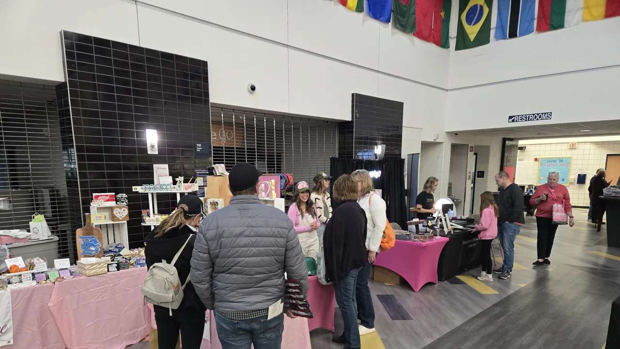 Shoppers browse vendor tables in a school commons hung with flags