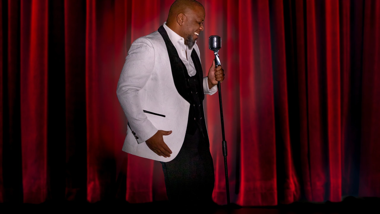 A singer in a white jacket stands at a vintage microphone before red curtains