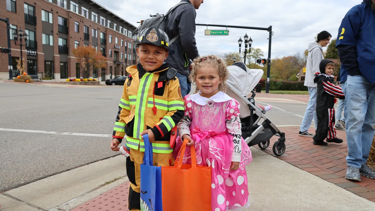 Small children in costumes trick-or-treat on a downtown sidewalk