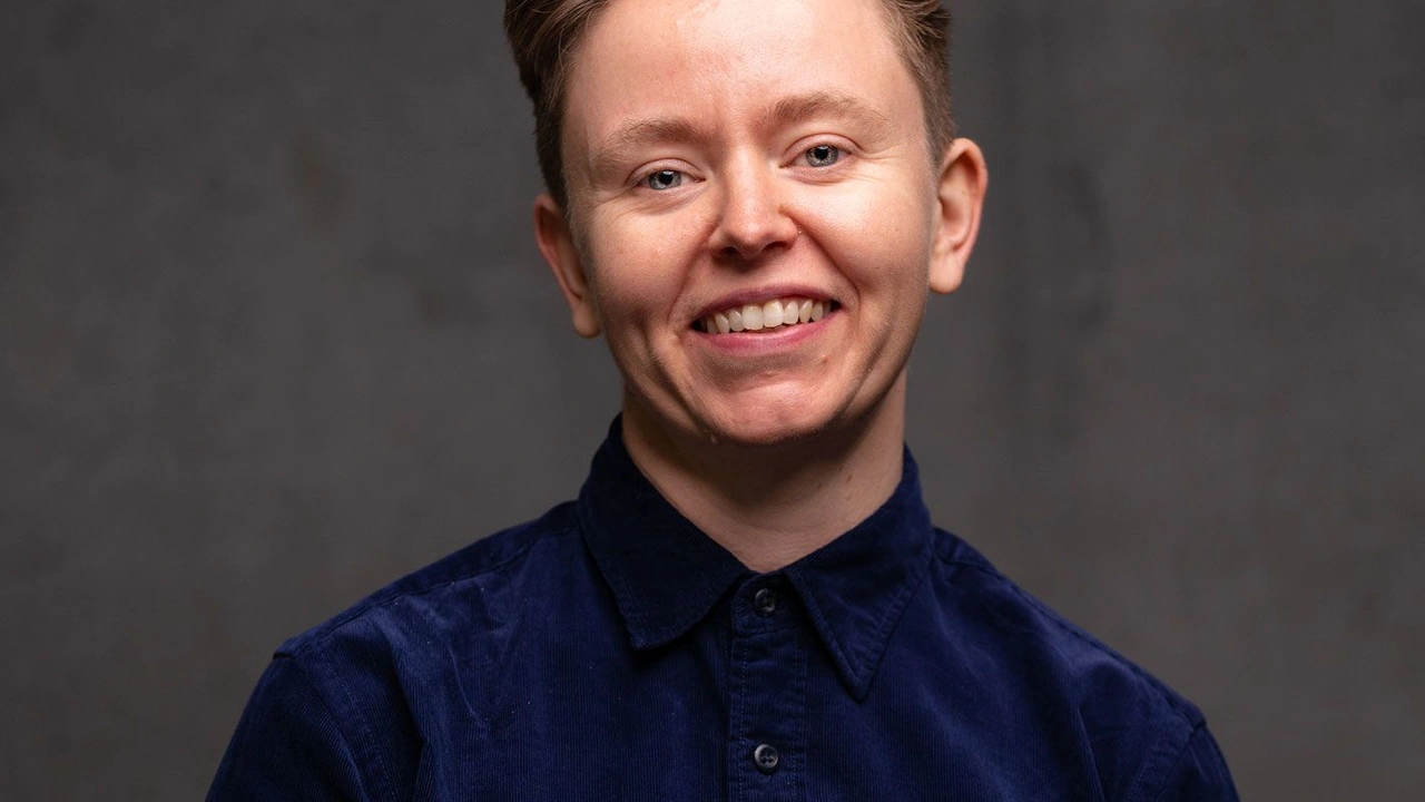 Portrait of a smiling person with short hair in a dark shirt