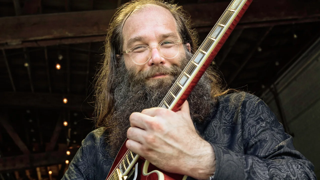 A bearded guitarist smiles with his electric guitar