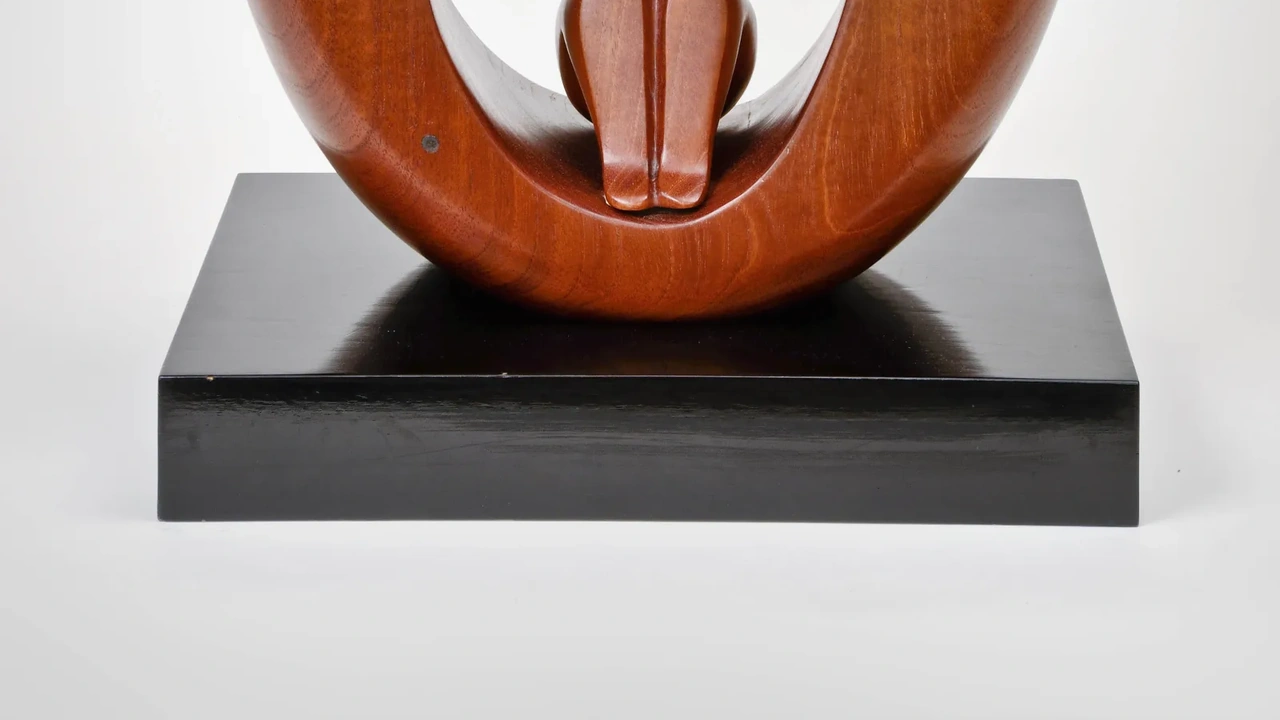 Polished red-brown wood sculpture with curving forms on a black pedestal.