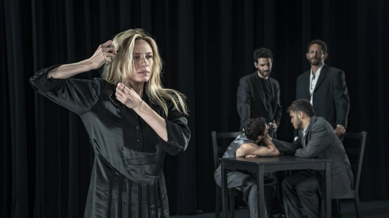 A dancer in black poses on stage as three men sit at a table behind her