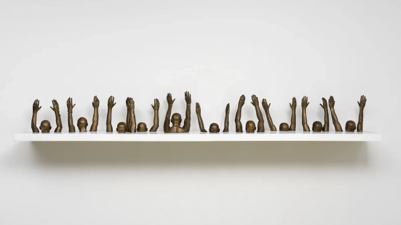 A row of small bronze raised-hand sculptures on a white gallery shelf