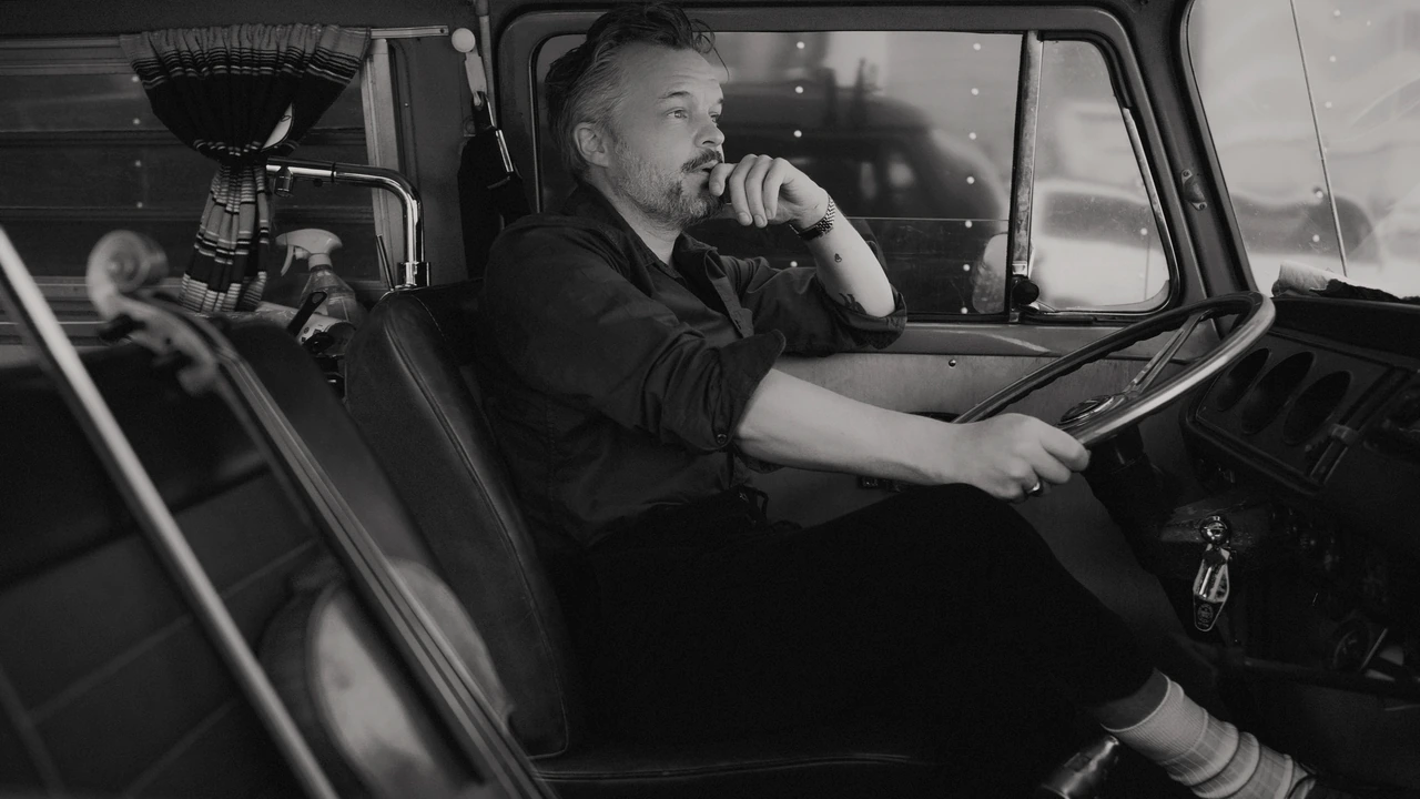A man sits at the wheel of an old truck in a black-and-white photo