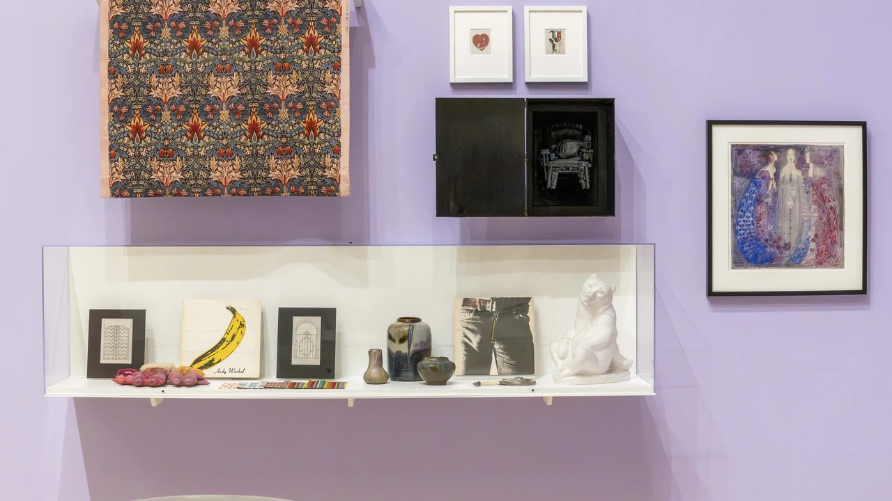 A lavender gallery wall with framed works, a patterned panel and a shelf of small objects.