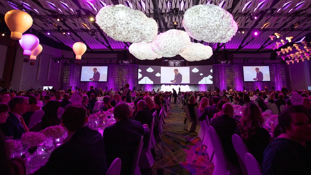 A ballroom lit in purple with cloud-like lights and seated guests
