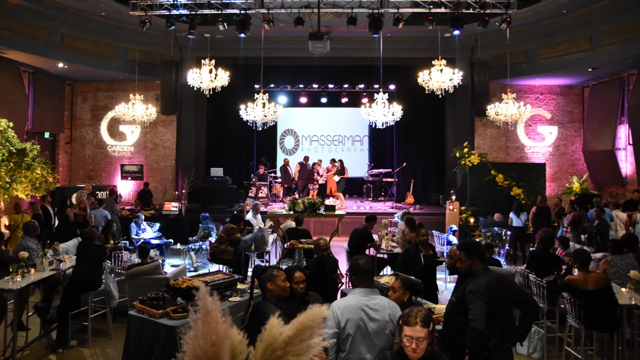 Guests fill a ballroom with chandeliers and a lit stage