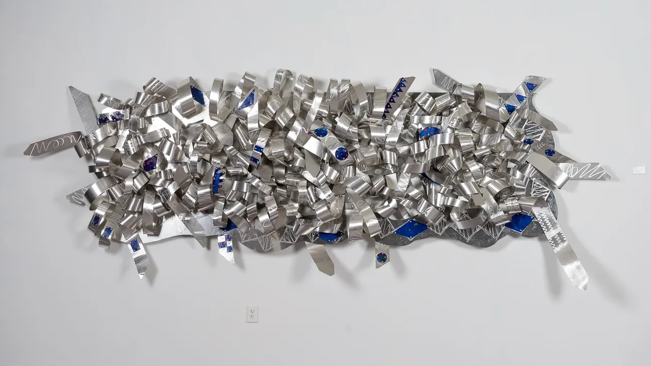 A sculpture of crumpled silver and blue foil pieces on a white wall