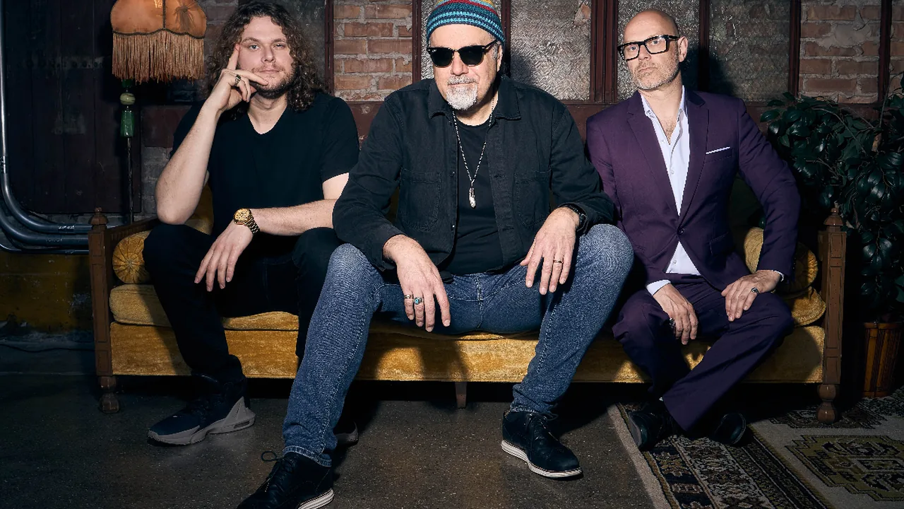 Three musicians sit on a couch in a dim lounge